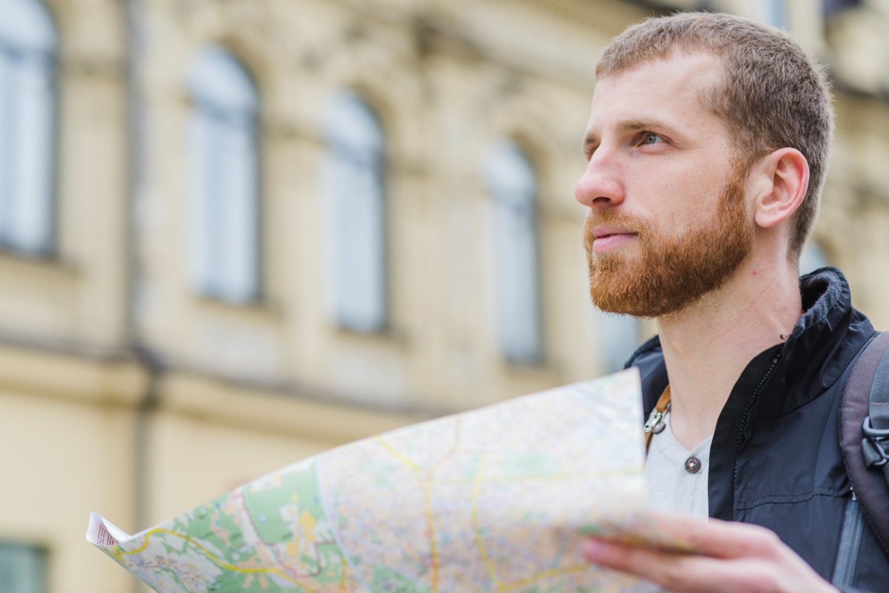 Junger Mann hält einen Stadtplan auf der Suche nach Orientierung