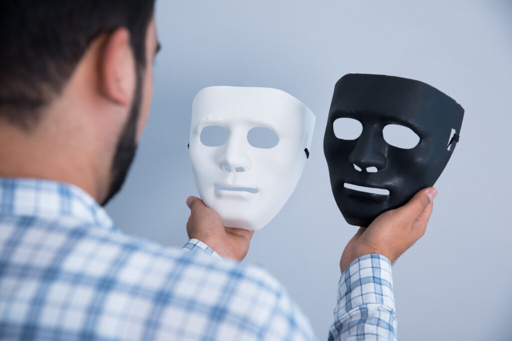 Mann hält eine weiße und eine schwarze Maske Sucht Symbolbild unsichtbare Gesichter der Betäubung