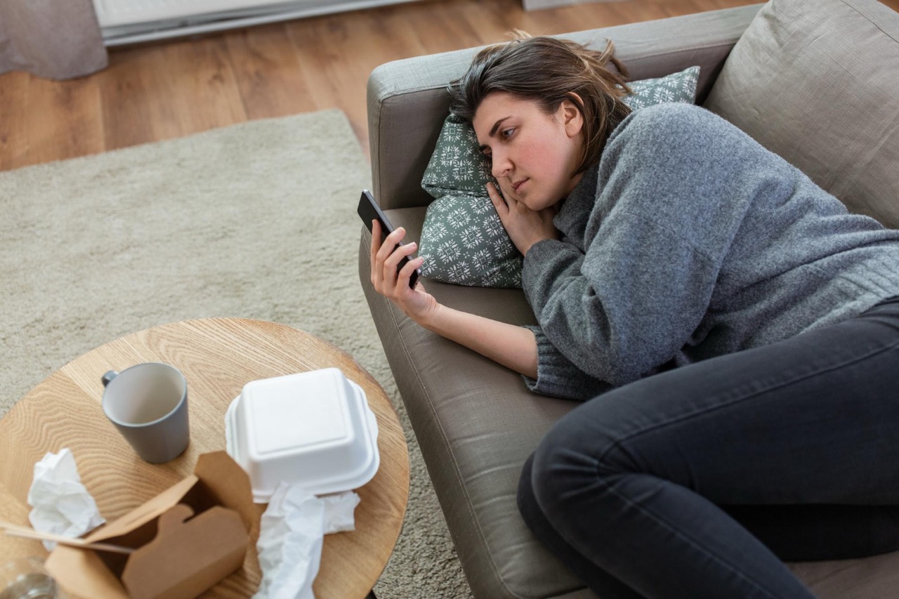 Eine junge Frau die auf der Couch ihr Handy in der Hand hält und soziale Medien nutzt Doomscrolling Symbolbild