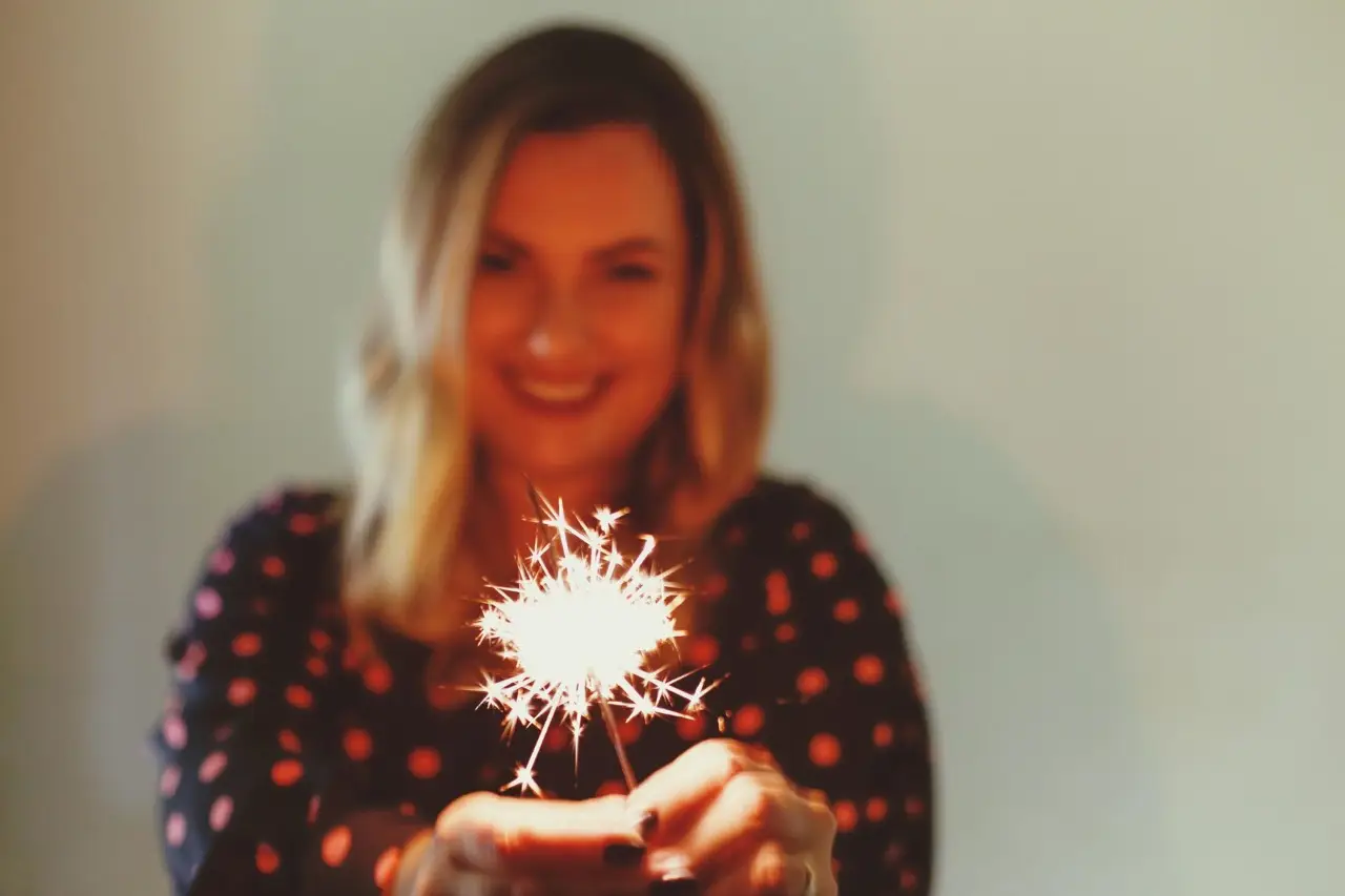 Lächelnde Frau hält eine brennende Wunderkerze in der Hand