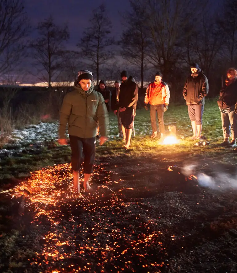 Menschen stehen abends um eine Feuerstelle beim Feuerlauf-Seminar