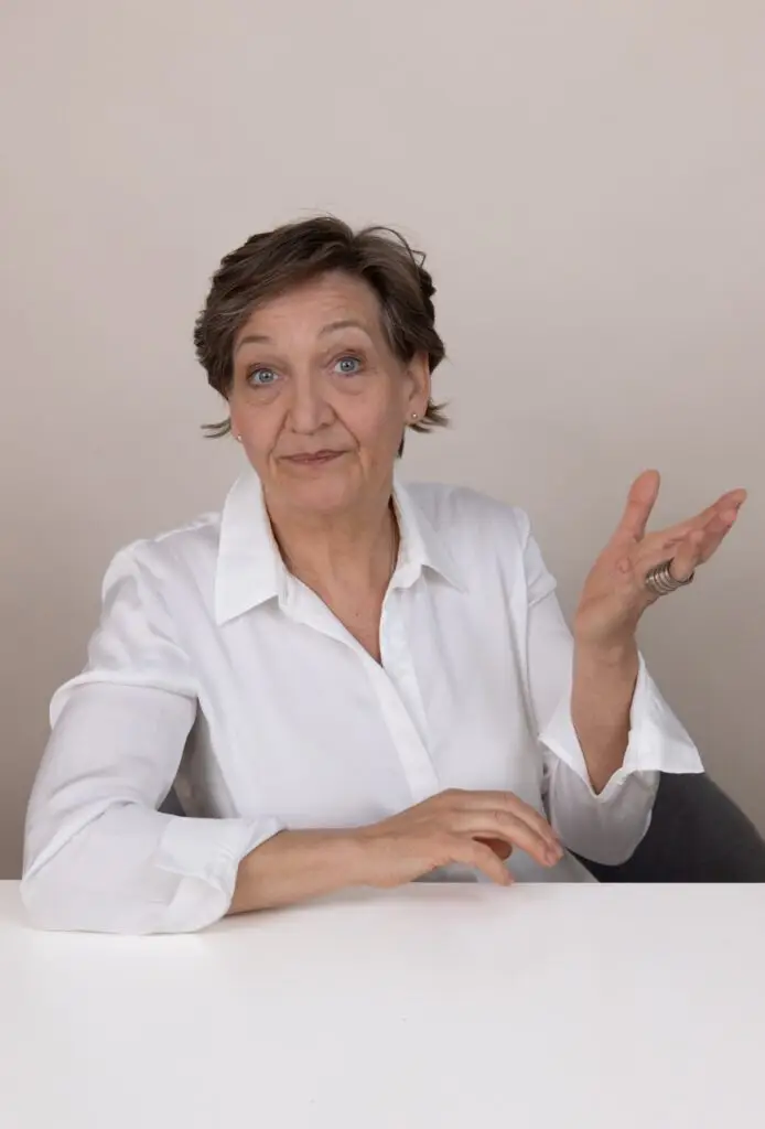 Andrea Däberitz sitzt im weißen Hemd am Tisch und gestikuliert fragend mit offenen Händen