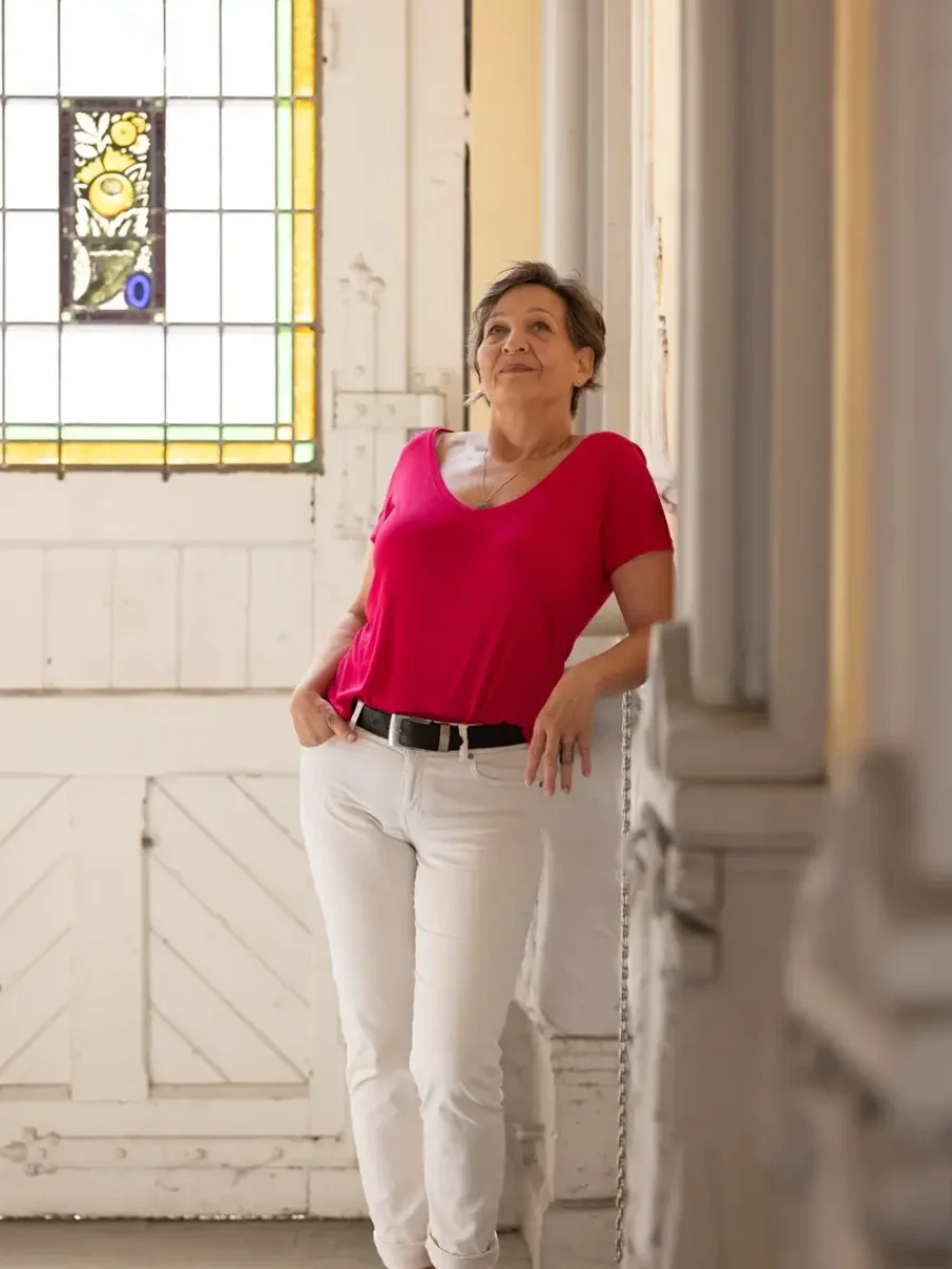 Andrea Däberitz lehnt lächelnd im roten Oberteil an einer Säule in einem hellen Saal