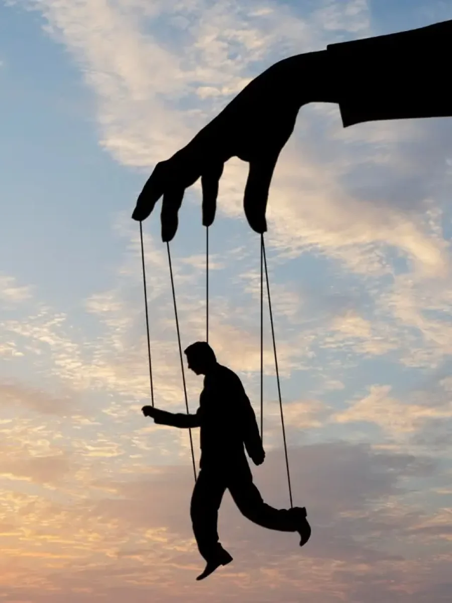 Riesige Hand führt eine Person wie eine Marionette an Fäden vor Abendhimmel